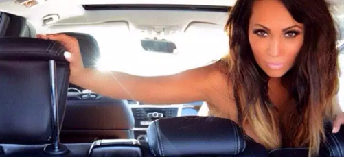 A woman sitting in the back of a car holding on to her steering wheel.